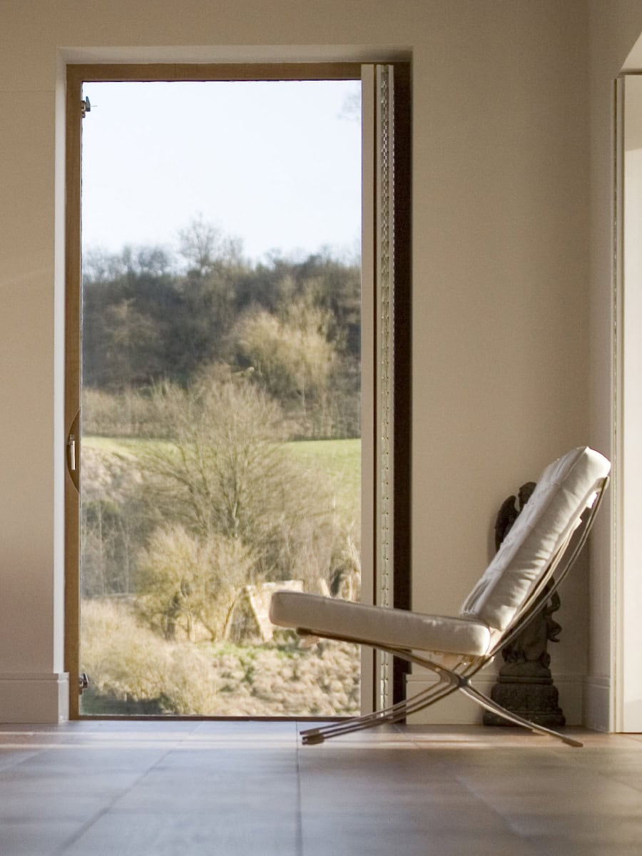 Barcelona chair beside floor-to-ceiling window framing Cotswold valley views at Vale Farm